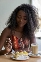 Portrait of young African woman eating a piece of cake and having a coffee - VEGF00700