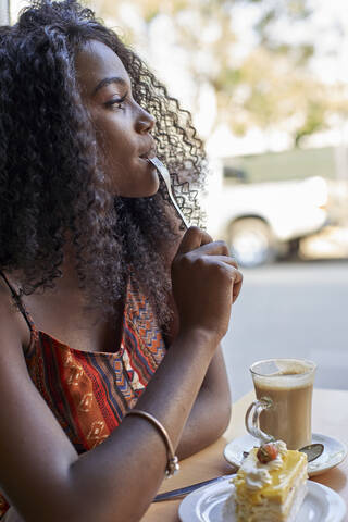 Porträt einer jungen Afrikanerin, die ein Stück Kuchen isst und einen Kaffee trinkt, lizenzfreies Stockfoto