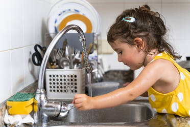 Kleines Mädchen wäscht das Geschirr im Küchenwasserhahn zu Hause - GEMF03139
