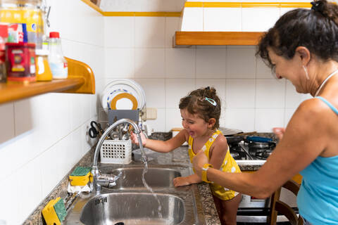 Kleines Mädchen und Großmutter spielen in der Küche mit Wasser, lizenzfreies Stockfoto
