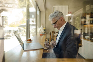 Senior businessman using cell phone in a cafe - GUSF02635