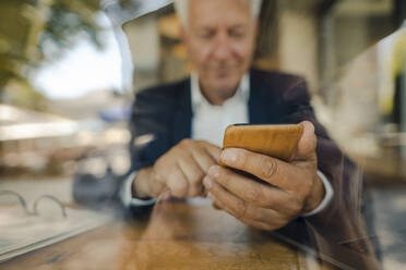 Ein älterer Geschäftsmann benutzt ein Handy in einem Café - GUSF02637