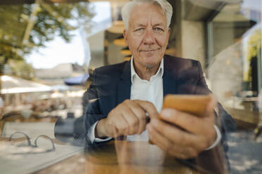 Porträt eines älteren Geschäftsmannes, der in einem Café ein Mobiltelefon benutzt - GUSF02638
