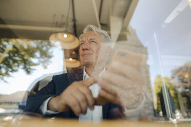 Senior businessman using cell phone in a cafe - GUSF02639