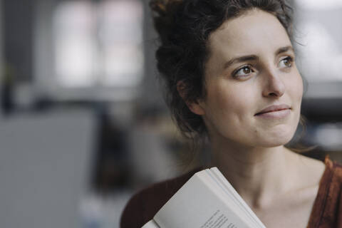 Portrait of smiling young woman with book looking at distance stock photo