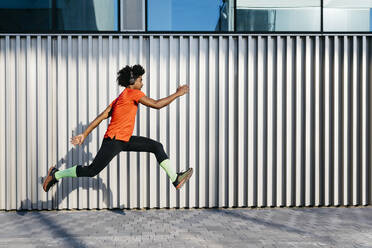 Junger Mann springt in der Stadt, Metallwand im Hintergrund - JRFF03711