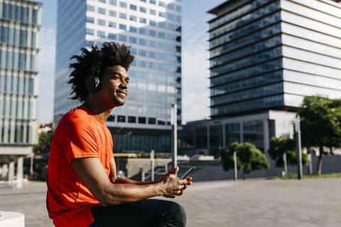 Young sportsman sitting on a bench, using smartphone and listening to music stock photo