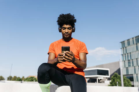 Young sportsman sitting on steps, using smartphone and listening to music stock photo