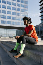 Young sportsman sitting on steps, using smartphone and listening to music - JRFF03729