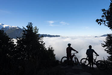 Mountain bikers look out across a valley filled with a cloud inversion in the Himalayas while biking in the Gosainkund region, Langtang region, Nepal, Asia - RHPLF09849