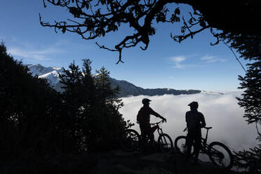 Mountain bikers look out across a valley filled with a cloud inversion in the Himalayas while biking in the Gosainkund region, Langtang region, Nepal, Asia - RHPLF09850