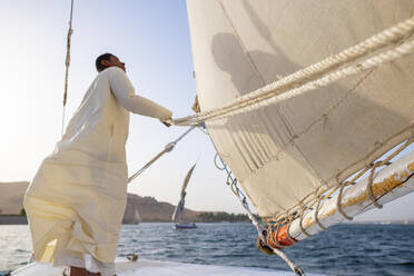 Ein ägyptischer Mann steht am Bug eines traditionellen Felucca-Segelboots mit Holzmasten und Baumwollsegeln auf dem Nil, Assuan, Ägypten, Nordafrika, Afrika - RHPLF09852