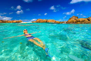 Schwimmbad an der Anse Cocos mit Frau im Bikini, die im türkisfarbenen Wasser des natürlichen Pools am Anse Cocos Beach liegt, geschützt durch Felsformationen, La Digue, Seychellen, Indischer Ozean, Afrika - RHPLF09857