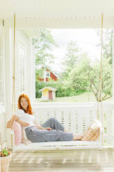 Woman sitting on swing in terrace - JOHF00300