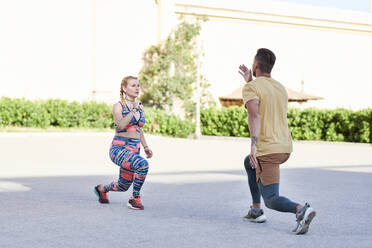 Fitnesstrainer beim Training mit einer jungen Frau im Freien in der Stadt - JNDF00089