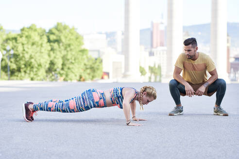 Fitnesstrainer beim Training mit einer jungen Frau im Freien in der Stadt - JNDF00090