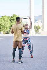 Fitness coach practicing with young woman outdoors in the city - JNDF00092