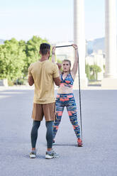 Fitnesstrainer beim Training mit einer jungen Frau im Freien in der Stadt - JNDF00092