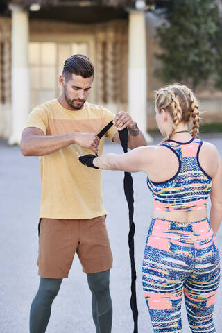 Fitnesstrainer, der mit einer jungen Frau im Freien in der Stadt Boxunterricht gibt und einen Verband anlegt, lizenzfreies Stockfoto
