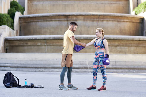 Fitness coach practicing boxing class with young woman outdoors in the city putting on boxing glove - JNDF00095