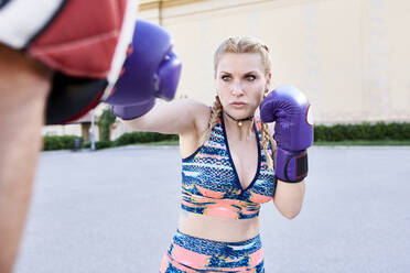 Konzentrierte junge Frau beim Boxen mit einem Fitnesstrainer im Freien in der Stadt - JNDF00098