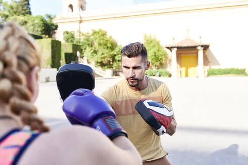 Fitnesstrainer, der mit einer jungen Frau im Freien in der Stadt Boxen übt - JNDF00099