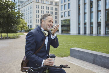 Älterer Geschäftsmann mit Fahrrad und Smartphone in der Stadt - RORF01851
