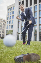 Glücklicher reifer Geschäftsmann spielt Golf auf dem Rasen in der Stadt - RORF01861