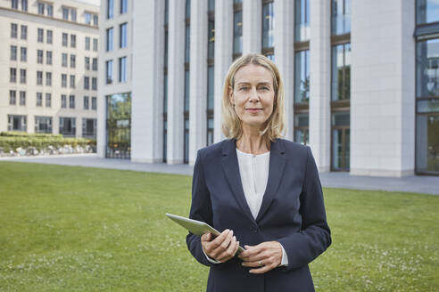 Porträt einer selbstbewussten Geschäftsfrau mit Tablet auf einer Wiese in der Stadt - RORF01870