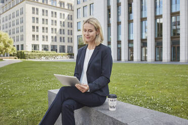 Businesswoman sitting on a wall in the city using tablet - RORF01872