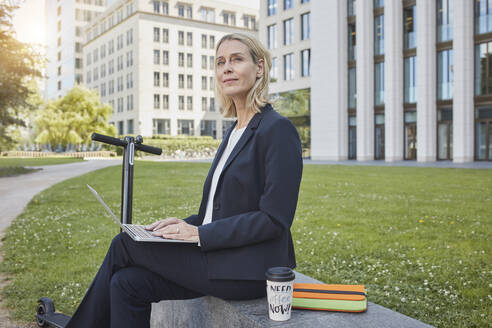 Geschäftsfrau sitzt auf einer Mauer in der Stadt und benutzt einen Laptop - RORF01876