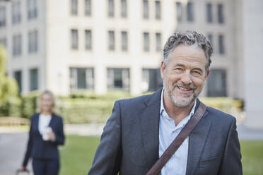 Porrait of smiling businessman in the city with businesswoman in background - RORF01883