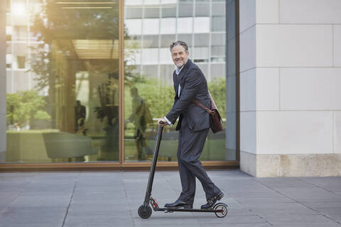 Businessman on e-scooter passing office building in the city stock photo