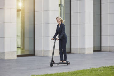 Geschäftsfrau auf E-Scooter beim Passieren eines Bürogebäudes in der Stadt - RORF01889