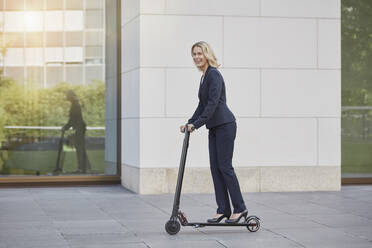 Geschäftsfrau auf E-Scooter beim Passieren eines Bürogebäudes in der Stadt - RORF01891