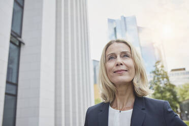 Porträt einer selbstbewussten blonden Geschäftsfrau in der Stadt mit Blick nach oben - RORF01894