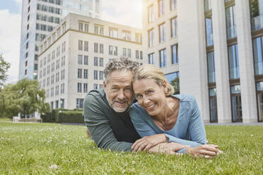 Portrait of happy mature couple lying on lawn in the city - RORF01926