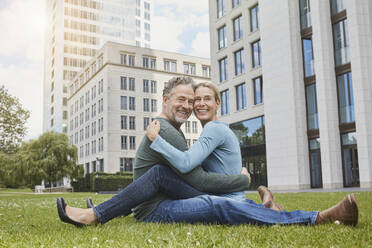 Glückliches reifes Paar sitzt auf dem Rasen in der Stadt - RORF01927