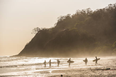 Surfer an einem Strand bei Sonnenuntergang, Nosara, Provinz Guanacaste, Pazifikküste, Costa Rica, Mittelamerika - RHPLF10355