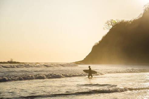 Surfer an einem Strand bei Sonnenuntergang, Nosara, Provinz Guanacaste, Pazifikküste, Costa Rica, Mittelamerika - RHPLF10358