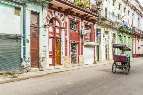 Eine alte Fahrrad-Rikscha, die an schöner lokaler Architektur in Havanna, Kuba, Westindien, Karibik, Mittelamerika vorbeifährt - RHPLF10482