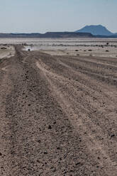 Geländewagen in der Ferne auf langer gerader Schotterstraße, blaue Berge im Hintergrund, nördlich von Solitaire, Namibia, Afrika - RHPLF10529