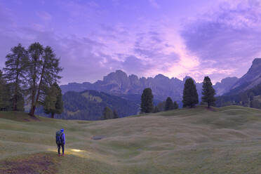 Wanderer betrachtet das rosa Licht der Abenddämmerung mit der Geislergruppe im Hintergrund, Wolkenstein, Grödnertal, Südtirol, Dolomiten, Italien, Europa - RHPLF10907