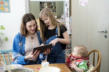 Mutter mit Tochter schaut auf ein digitales Tablet - JOHF00667