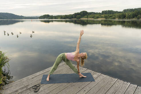 Young woman doing gymnastics on a jetty at a lake - JOSF03592