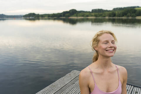 Smiling young woman with closed eyes on a jetty at a lake stock photo