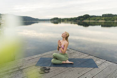 Young woman practicing yoga on a jetty at a lake - JOSF03605