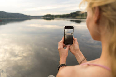 Junge Frau, die ein smartes Foto an einem See macht - JOSF03607