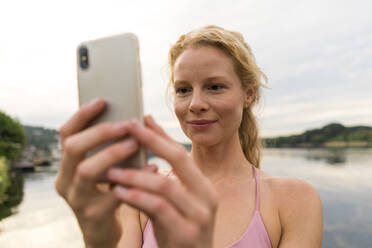 Junge Frau benutzt Mobiltelefon an einem See - JOSF03608