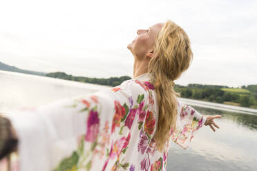 Happy young woman with outstretched arms at a lake - JOSF03622